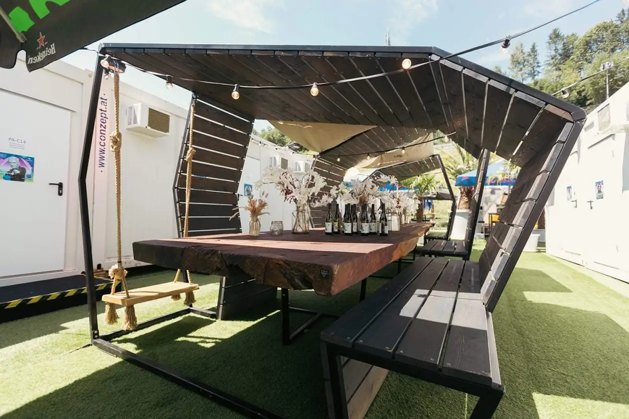 Dreikant Sitzbereich mit Massivholztischen unter der Pergola beim Electric Love Festival